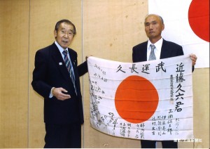 仲沢誠也本会常務理事から日章旗を受け取るご遺族の小畑久男さん（右）＝５月１１日、大館市中央公民館で