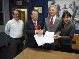 再委託契約を締結し、握手を交わす水落会長とジーク共同代表。右は敬子氏