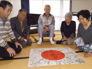 陸前高田市遺族会高田支部の皆さんへ日章旗を披露する津恵子さん（右端）